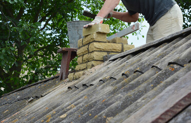 Chimney repair with laying new bricks. Building contractor is bricklaying new chimney pipe on old house with asbestos roof.