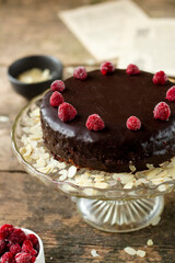 Traditional Austrian chocolate dessert, Sacher cake with frozen raspberries and almond slices  on a glass cake stand served on a wooden rustic table