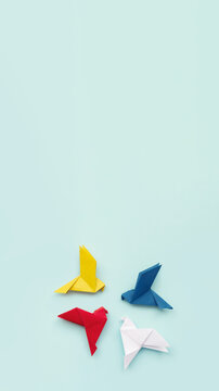 four paper origami pigeons red, blue, yellow and white on light background, vertical, 16:9