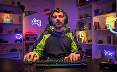 Happy gamer portrait playing games on the computer looking at camera while streaming gaming room.