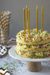 Birthday naked confetti cake with golden candles on a cake stand