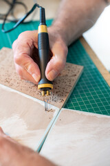 Close up man working with the pyrographer burning the wood making artwork craft in his art studio.