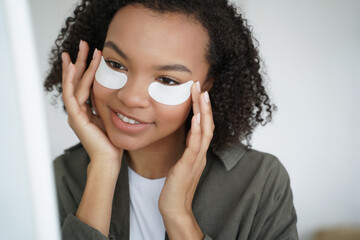 Happy pretty african american young girl applying moisturizing under eye patches. Skincare routine