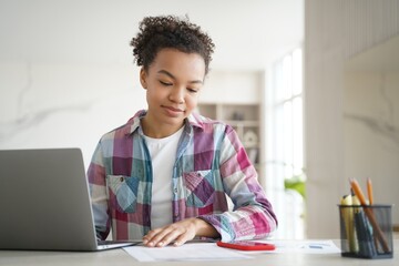 Mixed race teen student girl learning sitting at desk with laptop at home, preparing for school test