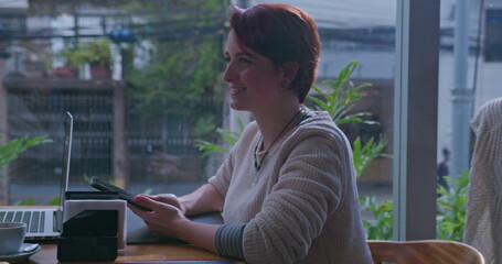 One young redhead woman seated at coffee shop speaking with friend off camera. Female red hair female person sitting by cafe window speaking