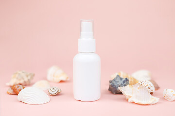 White cosmetic spray bottle and different sea shells a lot on pink background. Mockup branding. Skincare beauty and liquid antibacterial spray. Natural Body mist. Front view.