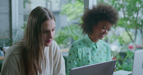 Two young women in front of laptop computers working. Female work colleagues collaborating at coffee shop