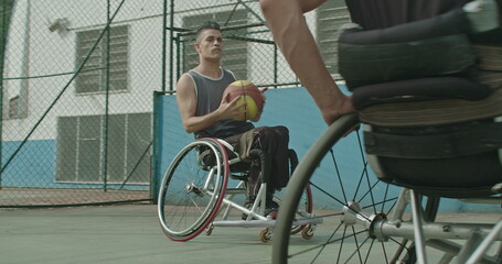 Two paraplegic disabled athletes playing basketball outdoors passing ball to team member. Determination and sport with disability concept