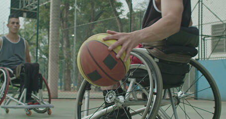 A paraplegic male athlete receiving ball from colleague outdoors. Two disabled athletes playing basketball in sport court outside. Sport and disability concept