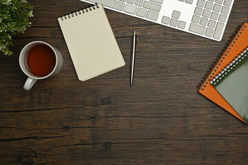 Wooden office desk with notepad, coffee cup, pen and potted plant. Top view with copy space