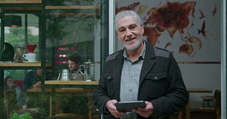 One happy business entrepreneur holding tablet looking at camera. A middled aged business owner smiling at camera portrait face