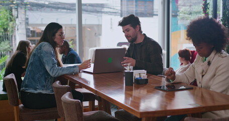 Male colleague showing laptop screen to female friend at coffee shop. Young man friend turning computer to woman sitting at cafe restaurant place. Group of people working remotely