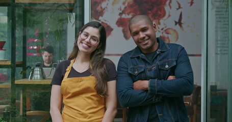 Fototapeta na wymiar Two diverse Brazilian hispanic employees of coffee shop portrait faces smiling. A black manager with a South American female staff standing in front of restaurant entrance