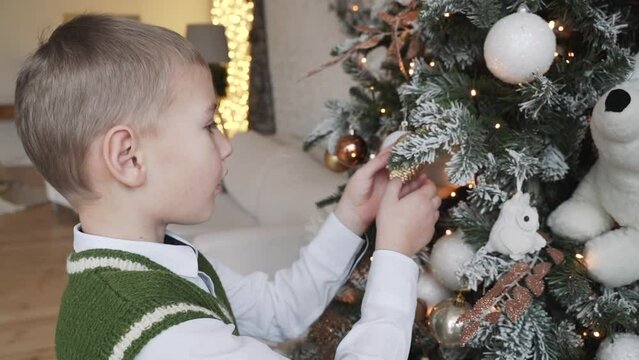 Happy little boy decorating Christmas tree with ball and background of lights