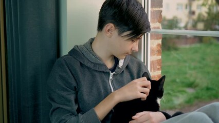 Boy looking out window. Handsome teenager with her cat sitting on windowsill in home from red bricks. Save lifes, no war, world peace, stop conflict, born love. Childhood in difficult times