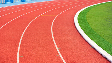 Empty red curve synthetic running tracks and green field in athletic outdoors stadium