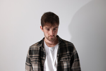 portrait d'un beau jeune homme de 25 ans debout, les mains dans les poches, portant une chemise. Sur fond gris