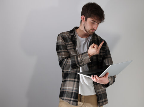 jeune homme debout, tenant un ordinateur portable et faisant un doigt d'honneur en regardant l'ordinateur