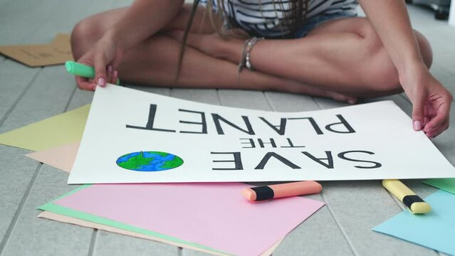 Close-up slow motion of female hands drawing posters banner im save the planet. Frame over shoulder.