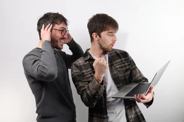 Foto op Plexiglas deux amis ou collègues sont debout avec un ordinateur portable. Ils serrent le poing en signe de réussite ou de victoire © Tof - Photographie