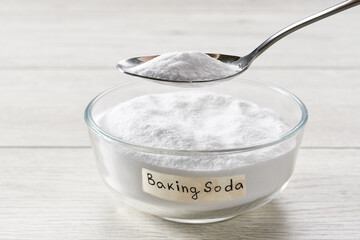 Close-up of baking soda on spoon against background of bowl on wooden table.