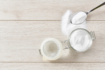 open jar of baking soda on a white kitchen table, top view.