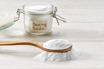 Baking soda in a wooden spoon on a light wooden table.