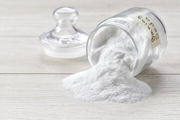 Baking soda spill out of a glass storage jar  on a white wooden table, selective focus.
