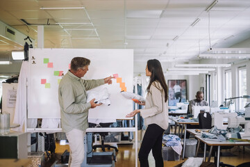 Side view of male fashion designer explaining female colleague on whiteboard at workshop