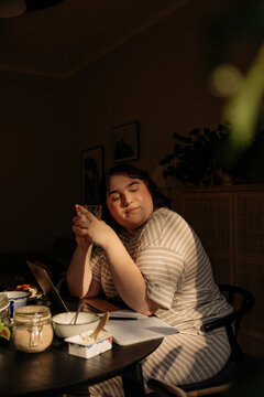 Young woman with eyes closed holding drinking glass while sitting at table