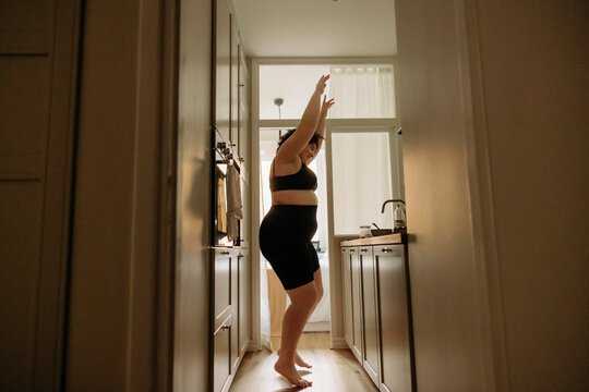 Young woman wit arms raised enjoying dance in kitchen at home