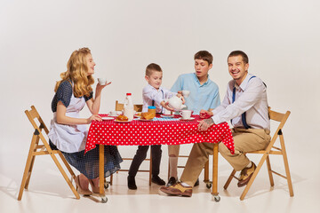 Portrait of lovely young family, woman, man and two boys sitting at the table and having breakfast...