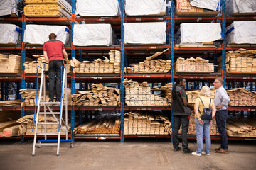 Saleswoman assisting customers while salesman standing on ladder at hardware store