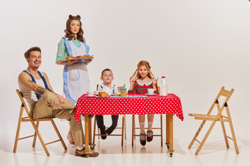 Portrait of beautiful young family sitting at the table and having breakfast together over grey background