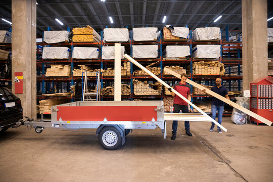 Salesman and male customer loading planks in trailer at hardware store