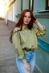 Fototapeta premium Young woman with long ginger hair outdoors in city. Young woman face with freckles