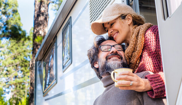 Romantic feeling moment with man and woman in tenderness outside a camper van with forest trees in background. Concept of happy and free lifestyle vacation for people. Man and woman in love outdoor - Powered by Adobe