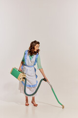 Portrait of young beautiful woman cleaning house with vacuum cleaner isolated over grey background