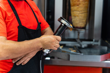 Chef of the kebab restaurant, using the electric tool to cut doner meat from the grill