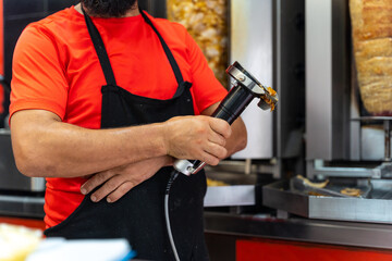Chef of the kebab restaurant, using the electric tool to cut doner meat from the grill