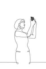 woman standing holding phone in her hands - one line drawing vector. the concept of taking a photo or trying to catch a communication signal
