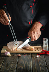 Chef cuts the chicken leg with a knife in the kitchen. The concept of a recipe for a delicious chicken meal with spices for a hotel or restaurant