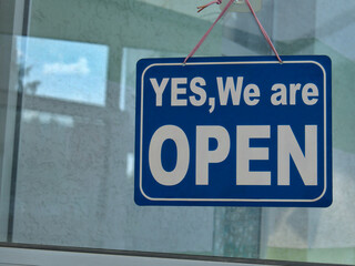 A "Yes, We are OPEN" sign hanging on the store's glass door