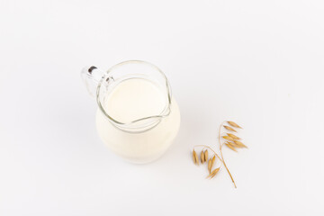 Oat milk in a jug and oat spike on light background. Vegan non dairy alternative milk.