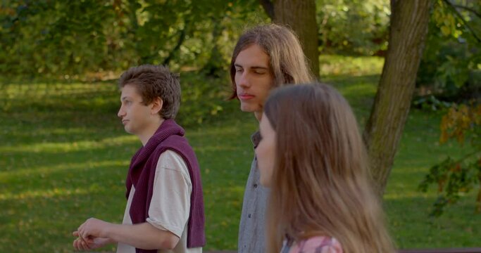 Two boys and girl. Polyamory is engaging in multiple romantic relationships. Three young people are walking through the park, talking. Effective communication in love triangle. Romance of student life
