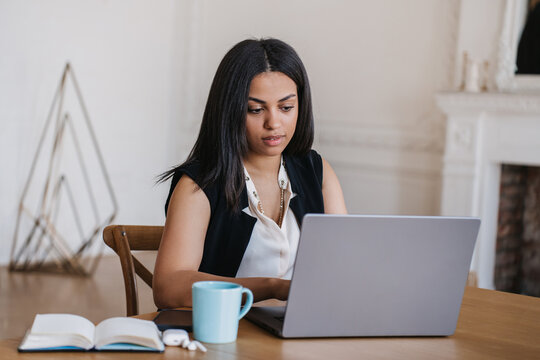 Attractive African American young woman sitting at desk using laptop at home. Attractive Brazilian student girl learning via internet, having distant lesson. Education and business.