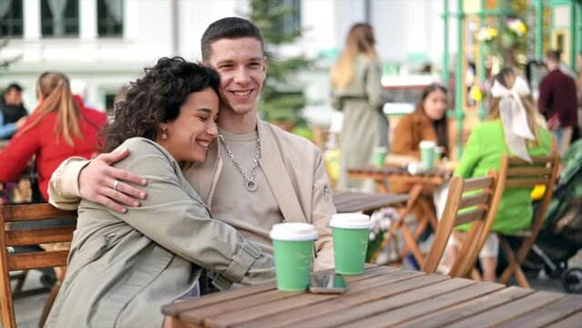 A happy couple outdoors near a cafe. Hugging each other, smiling, coffee. Autumn atmosphere. Slow motion