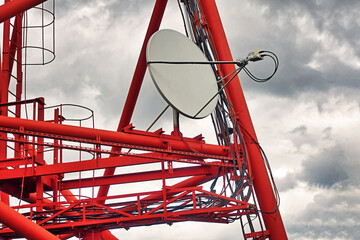 Part of communication tower with satellite dish against backdrop of dramatic sky with storm clouds. Telecommunication tower close-up.