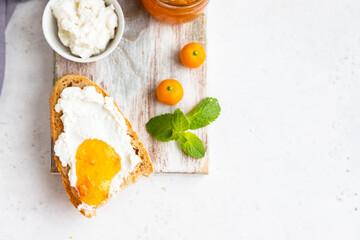 Sliced artisan homemade bread with ricotta or cottage cheese and orange jam on light background....