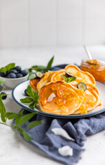 Traditional fluffy pancakes with orange jam, blueberries, coconut chips and mint for healthy breakfast, light background. High key photography.